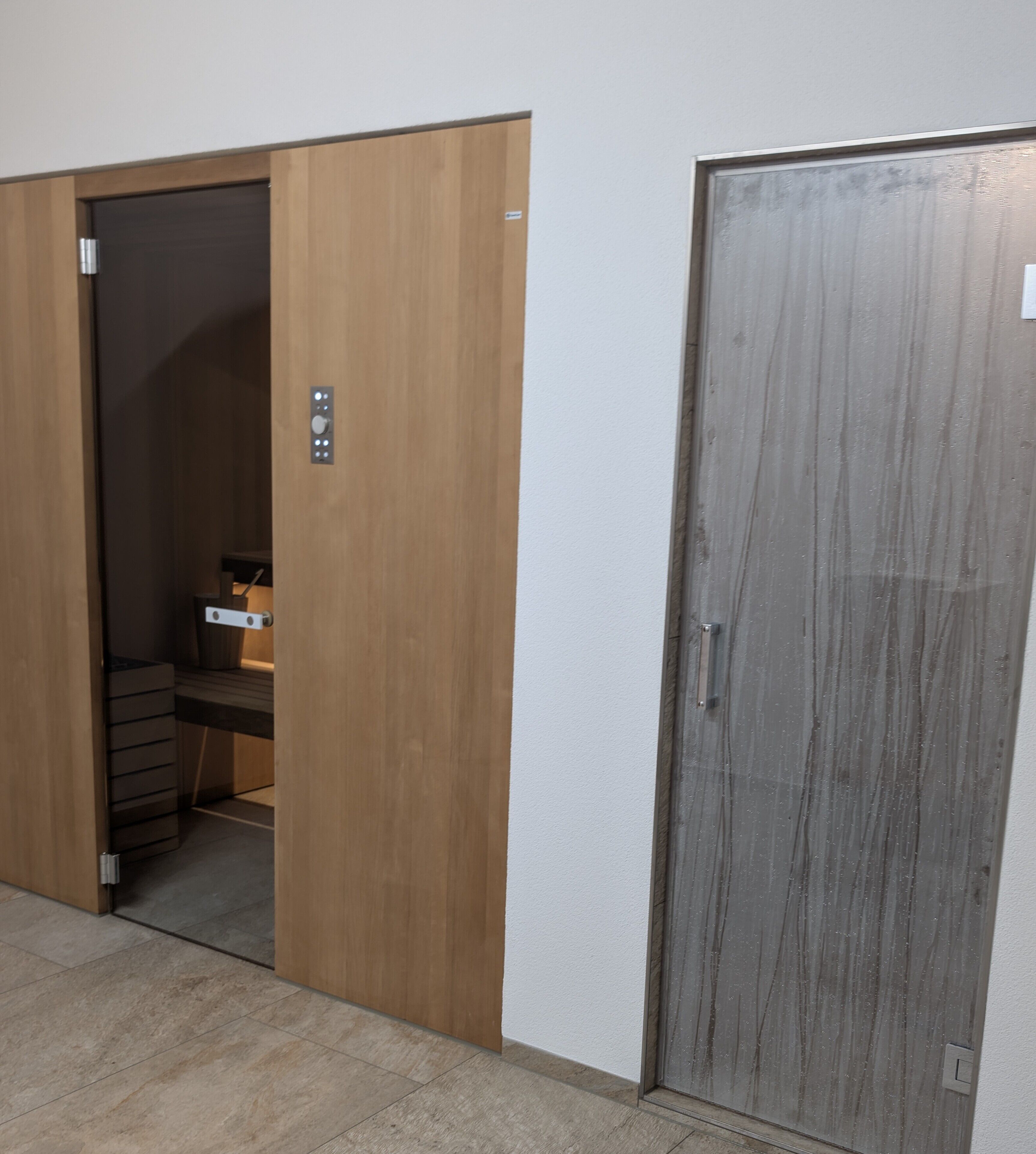 A room with a wooden wardrobe, a closed grey door, and a tiled floor.