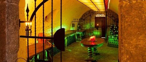 An underground passageway with stone walls, a metal gate, and a table with a candle.