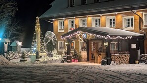 Un hotel con entrada cubierta de nieve, un árbol de Navidad y mesas al aire libre.