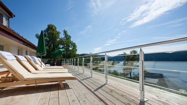 Terraza de madera con sillones de descanso y sombrillas con vista a un lago.