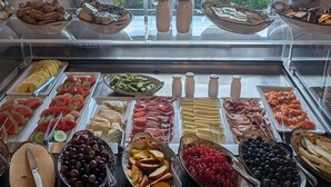 Un bufé con diversos alimentos, entre ellos frutas, quesos y carnes, expuestos en estantes de vidrio.