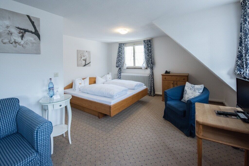 A bedroom with a bed, a chair, a small table, a radiator, and a window with curtains.