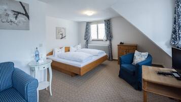 A bedroom with a bed, a chair, a small table, a radiator, and a window with curtains.