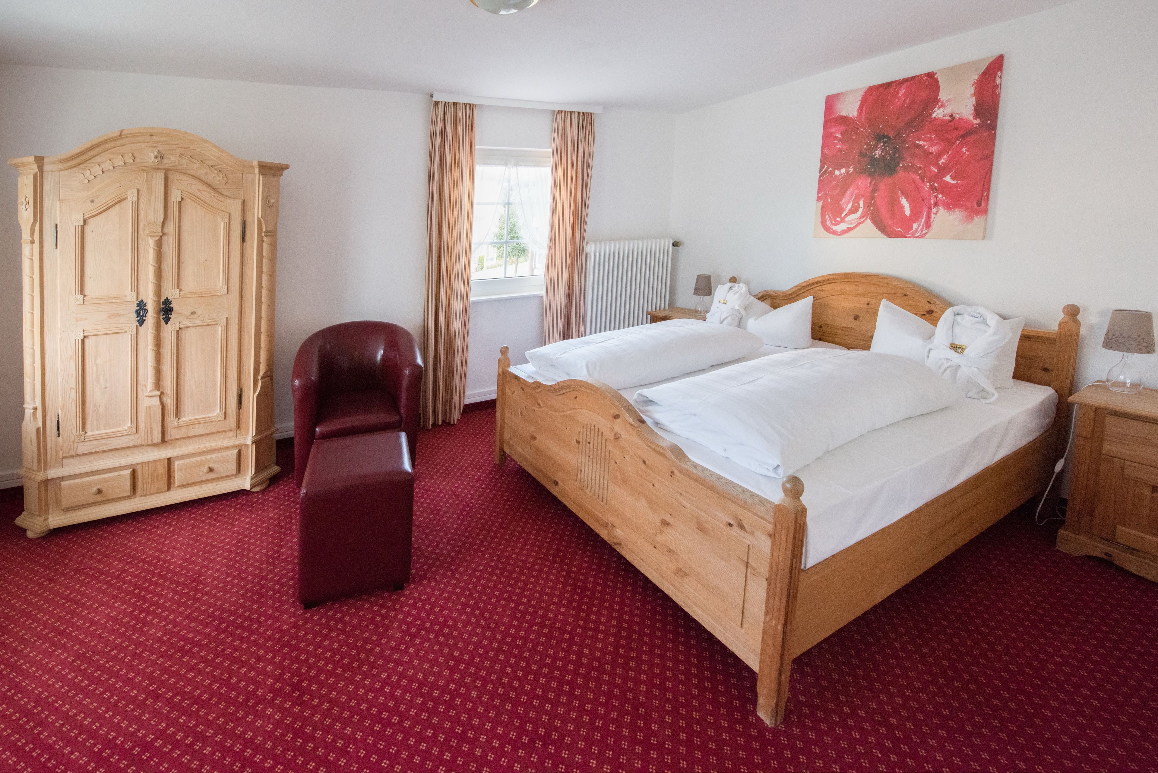Un dormitorio con una cama de madera, un armario de madera, un sillón rojo y una alfombra roja.