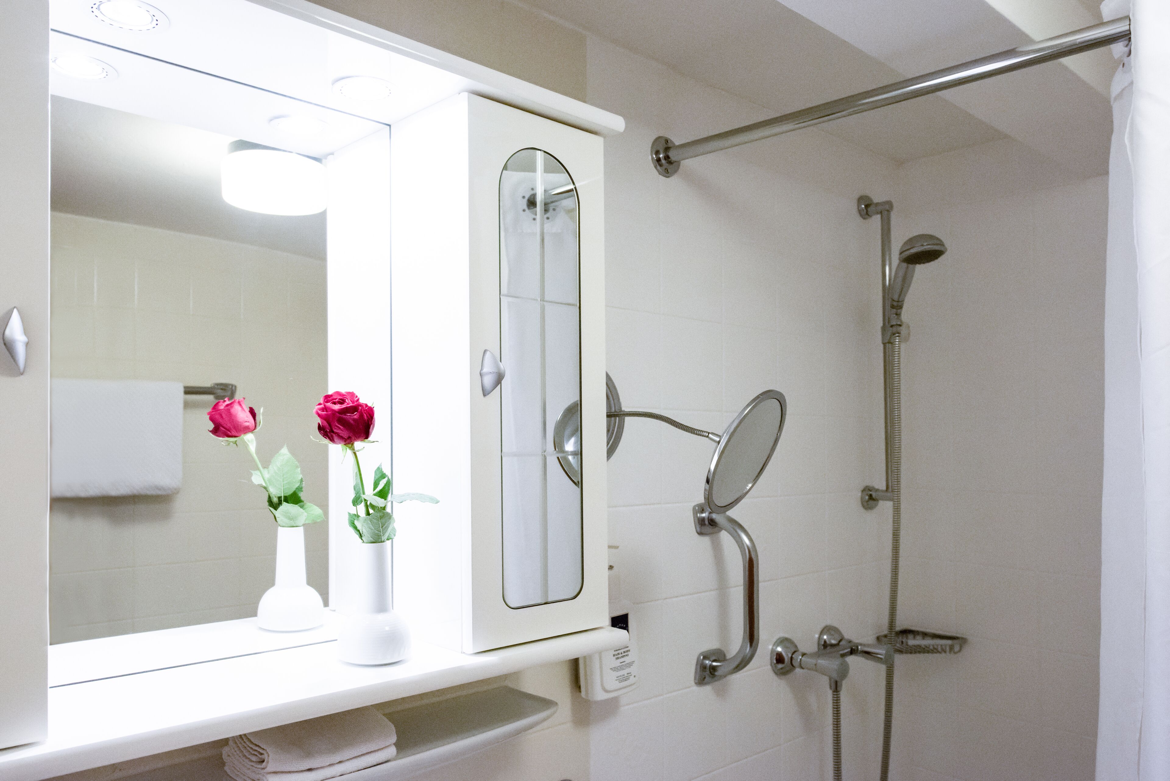 A bathroom with a shower, a mirror, and two vases with flowers.