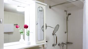 A bathroom with a shower, a mirror, and two vases with flowers.