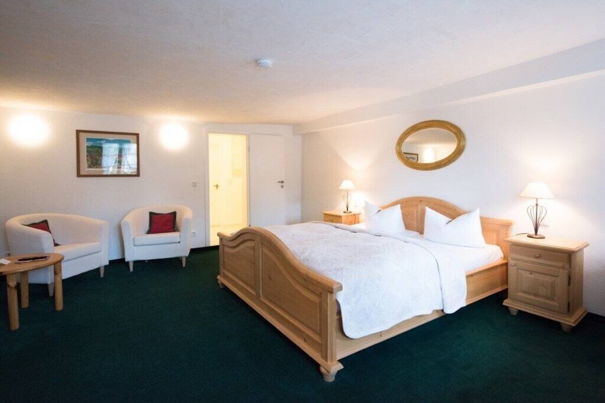 Un dormitorio con una cama de madera, dos mesitas de noche con lámparas, una silla, una pequeña mesa y una puerta.