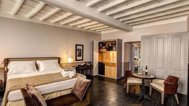 A hotel room with a large bed, a small dining table, a kitchen area, and a separate seating area with chairs. - Suite Giulia 2 (Rome)