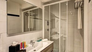 A modern bathroom with a glass-enclosed shower, a large mirror, and a white sink with toiletries. - Suite Giulia 2 (Rome)