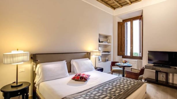Una habitación de hotel con cama, lámpara de noche, televisor y una pequeña mesa con una silla.