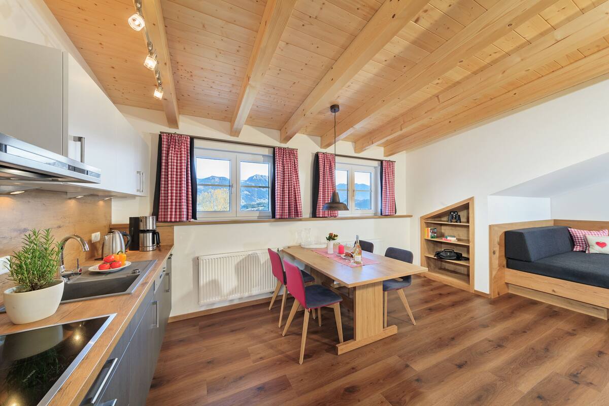 A modern kitchen with wooden beams, a dining table, chairs, and a sofa.