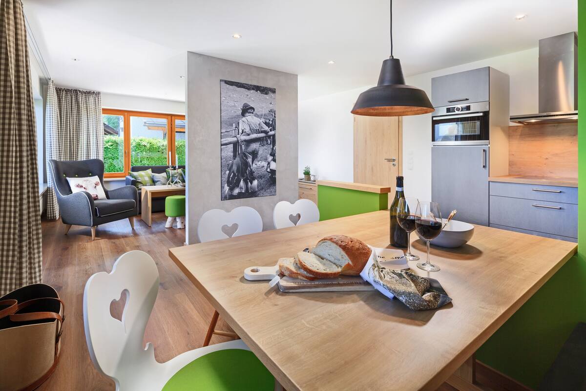 A modern kitchen with a wooden table, a hanging light, and a refrigerator.