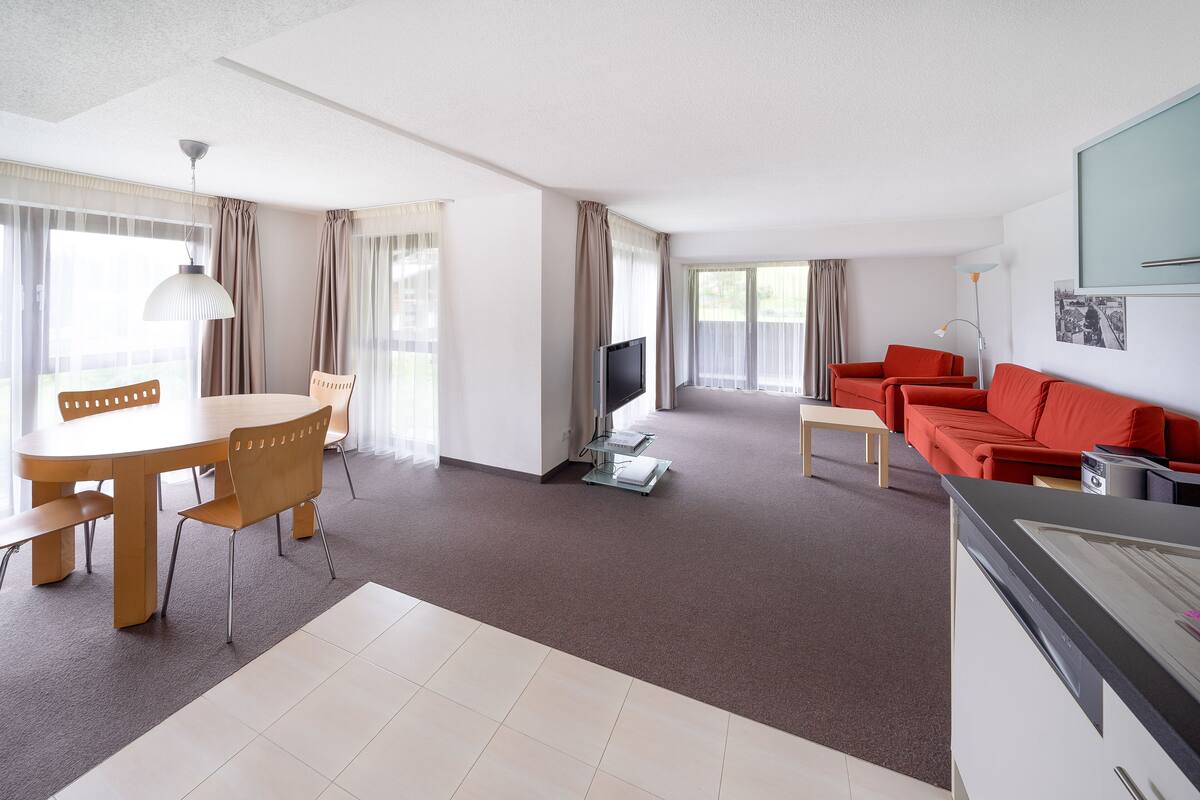 A modern living room with a dining area, red sofa, flat-screen TV, and a kitchen area.