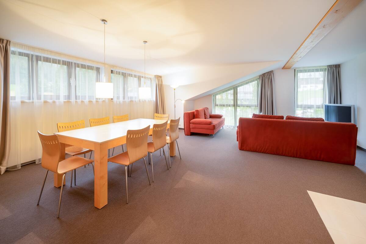 A spacious room with a dining table and chairs, a red sofa, and a television.