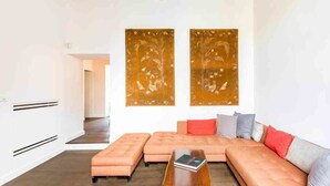 Una sala de estar moderna con un sofá modular, otomanas y una mesa de centro. Dos grandes obras de arte decoran la pared sobre el sofá.
