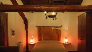 Un dormitorio con una cama de madera, dos lámparas de noche, un armario de madera y un techo inclinado con vigas a la vista.