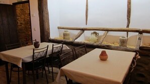 Un comedor rústico con mesas y sillas de madera, una pared de piedra y vistas a una oveja a través de una cerca de madera.