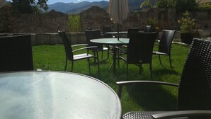 Un patio al aire libre con mesas y sillas redondas, un paraguas colgante y vistas a montañas al fondo.