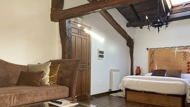 Una habitación acogedora con techo de madera, una cama con colchón blanco, un sofá marrón y una mesa de centro de vidrio.