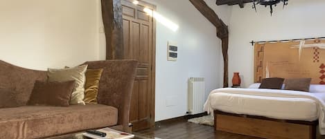 A cozy room with a wooden ceiling, a bed with a white mattress, a brown sofa, and a glass coffee table.