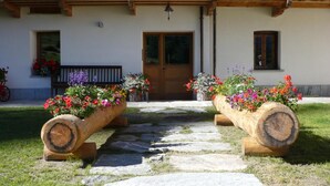 A building with a wooden balcony, a stone pathway leading to a wooden door, and flower planters on either side. - Dresalwoald (Gressoney-Saint-Jean)