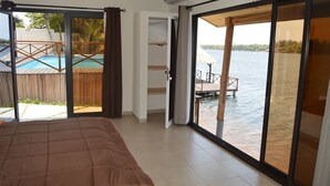 Un dormitorio con una cama grande, un ventanal corredero que da a un balcón con piscina y vistas al agua.