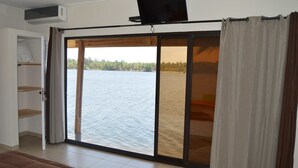 Una habitación con puerta de vidrio corredera que da a una vista del lago, un televisor de pantalla plana montado sobre la puerta y una pequeña estantería a la izquierda.