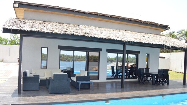 Zona junto a la piscina con una estructura de techo de paja, asientos al aire libre y vista al mar.