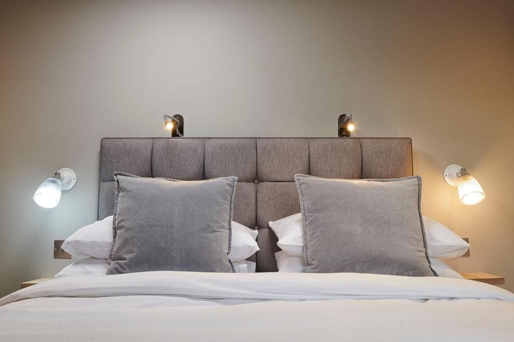 Una cama bien hecha con un cabecero, dos lámparas de pared y una mesita de noche.