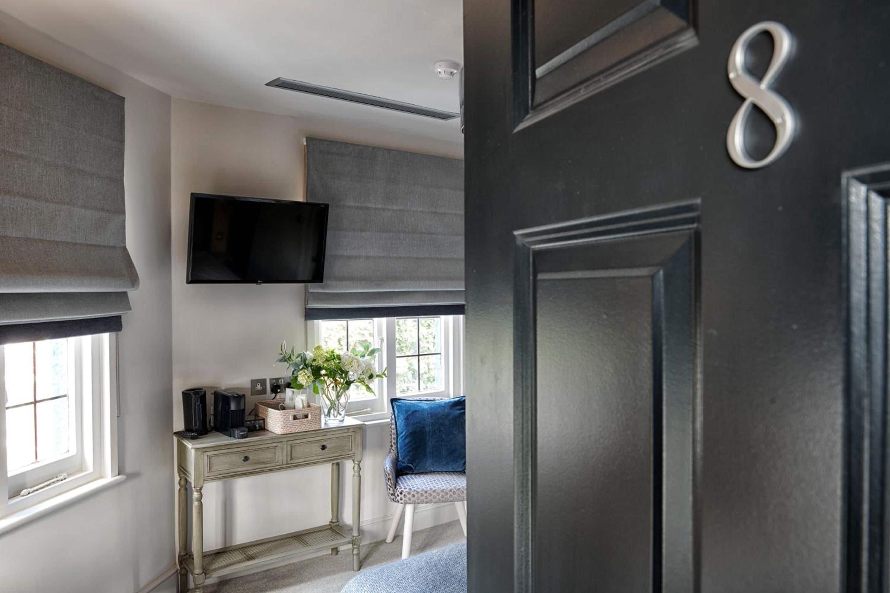 A room with a desk, a chair, a television mounted on the wall, and a door with a number.