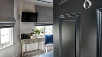 A room with a desk, a chair, a television mounted on the wall, and a door with a number.
