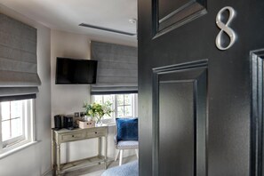 A room with a desk, a chair, a television mounted on the wall, and a door with a number. - The Bridge in Barnes (London)