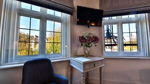 Une pièce dotée d’une grande fenêtre, d’un téléviseur à écran plat fixé au mur, d’une chaise et d’une petite table sur laquelle est posé un vase de fleurs.