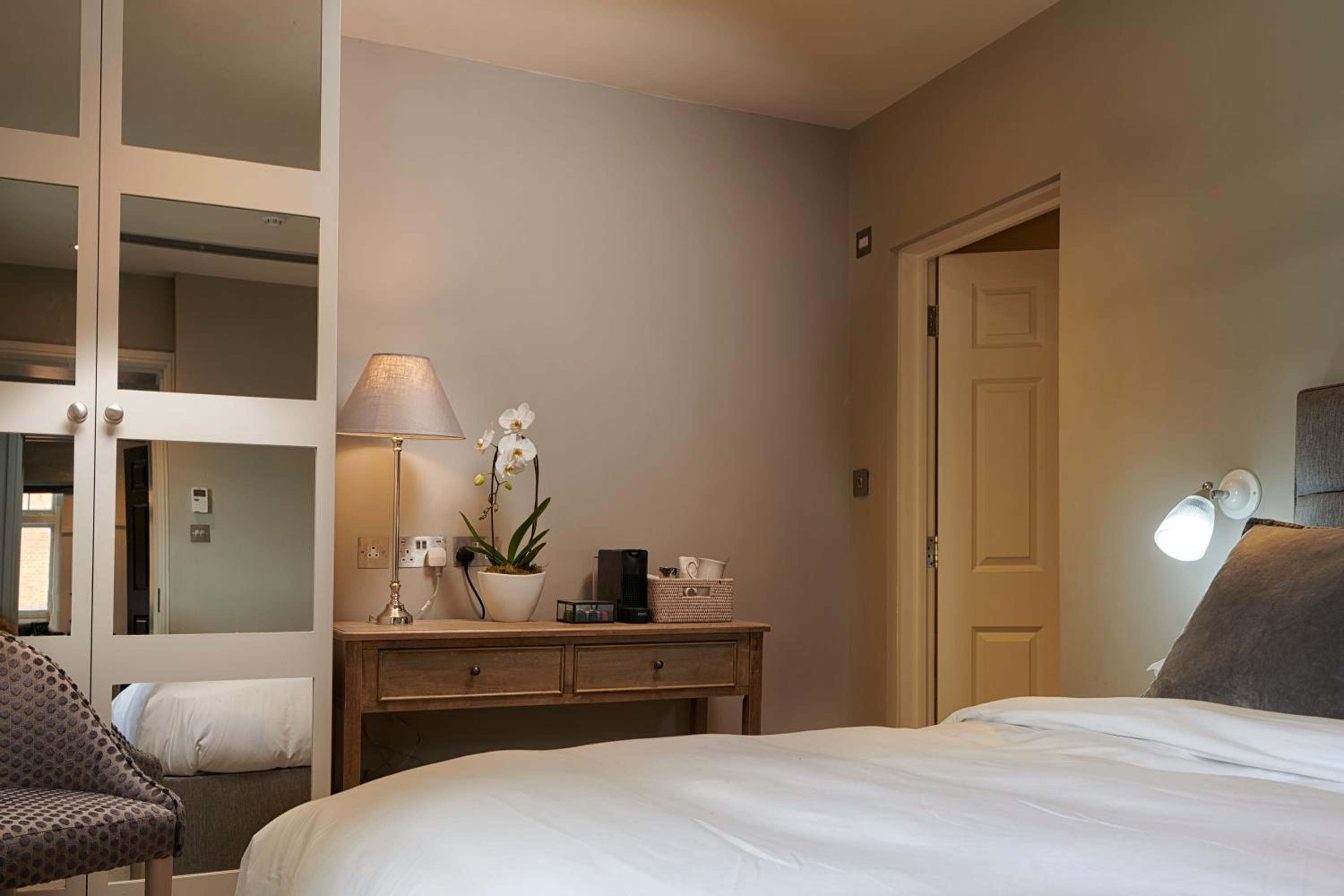 A hotel room with a bed, a desk with a lamp, an orchid, and a wall-mounted light fixture.