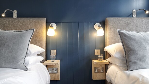 Une chambre d’hôtel avec deux lits, chacun doté d’une tête de lit, de tables de chevet, de lampes et d’oreillers.
