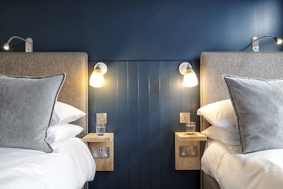 Ein Hotelzimmer mit zwei Betten, jeweils mit Kopfteil, Nachttischen, Lampen und Kissen.