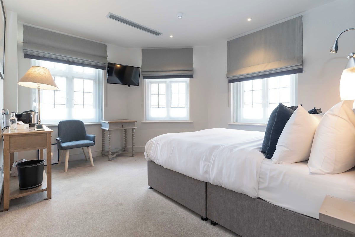 Ein Hotelzimmer mit Bett, Schreibtisch mit Stuhl, Wandfernseher und großen Fenstern mit Vorhängen.