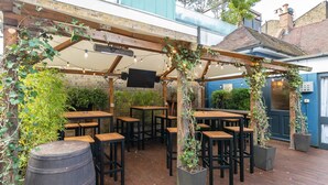 Un espace extérieur aménagé en terrasse, avec des tables et des chaises en bois, un grand tonneau et des plantes en pot.