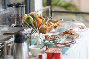 Un bufé con diversos alimentos y utensilios, que incluye frutas, pasteles y salsas.