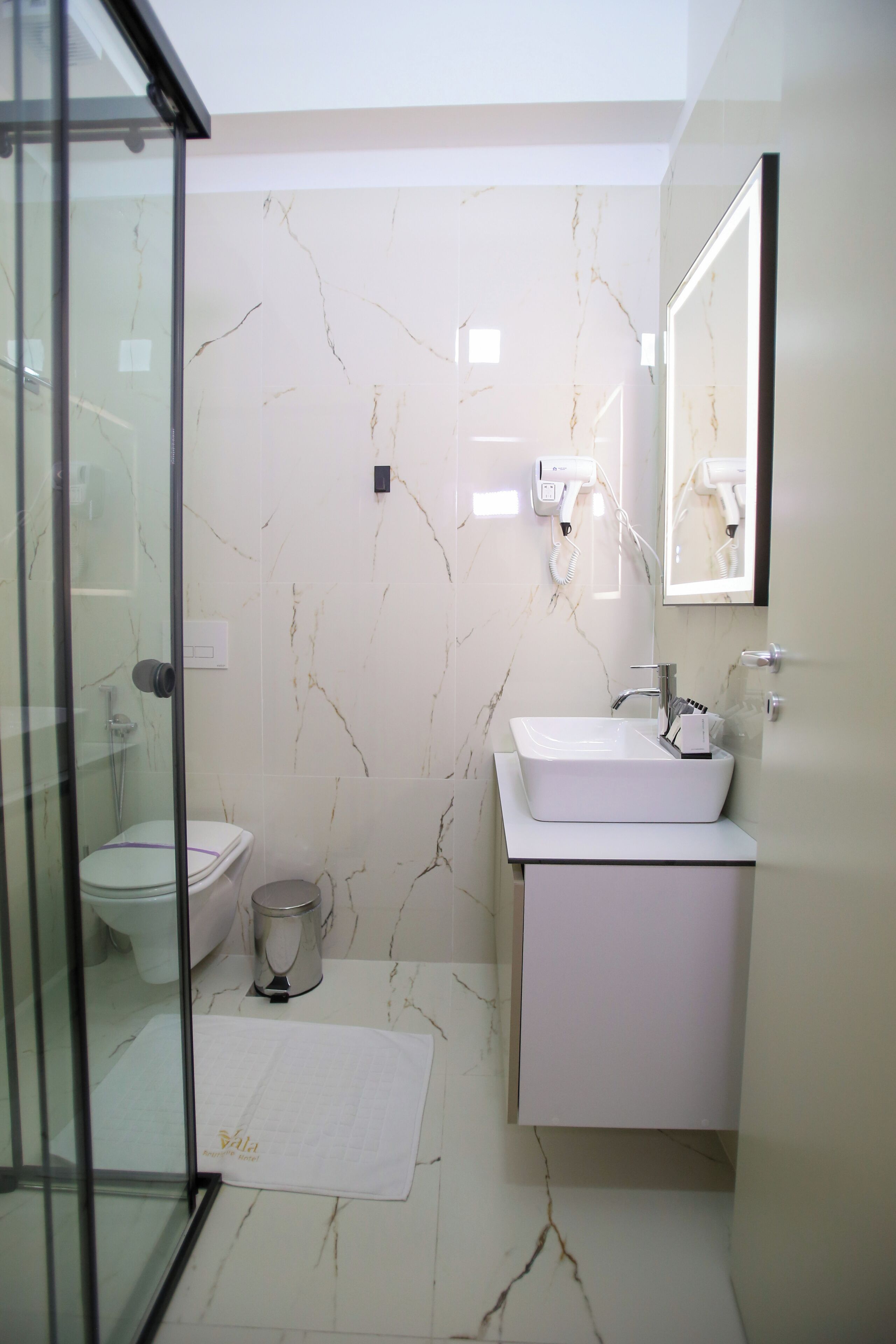 A modern bathroom with a glass shower enclosure, a white sink, and a marble backsplash.