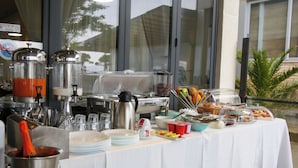Montaje de bufé con diferentes alimentos y bebidas, que incluye una máquina de café, dispensador de bebidas calientes y una variedad de platos y aperitivos.
