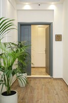 Zona de recepción de hotel con una puerta cerrada, plantas en macetas y el letrero de recepción.