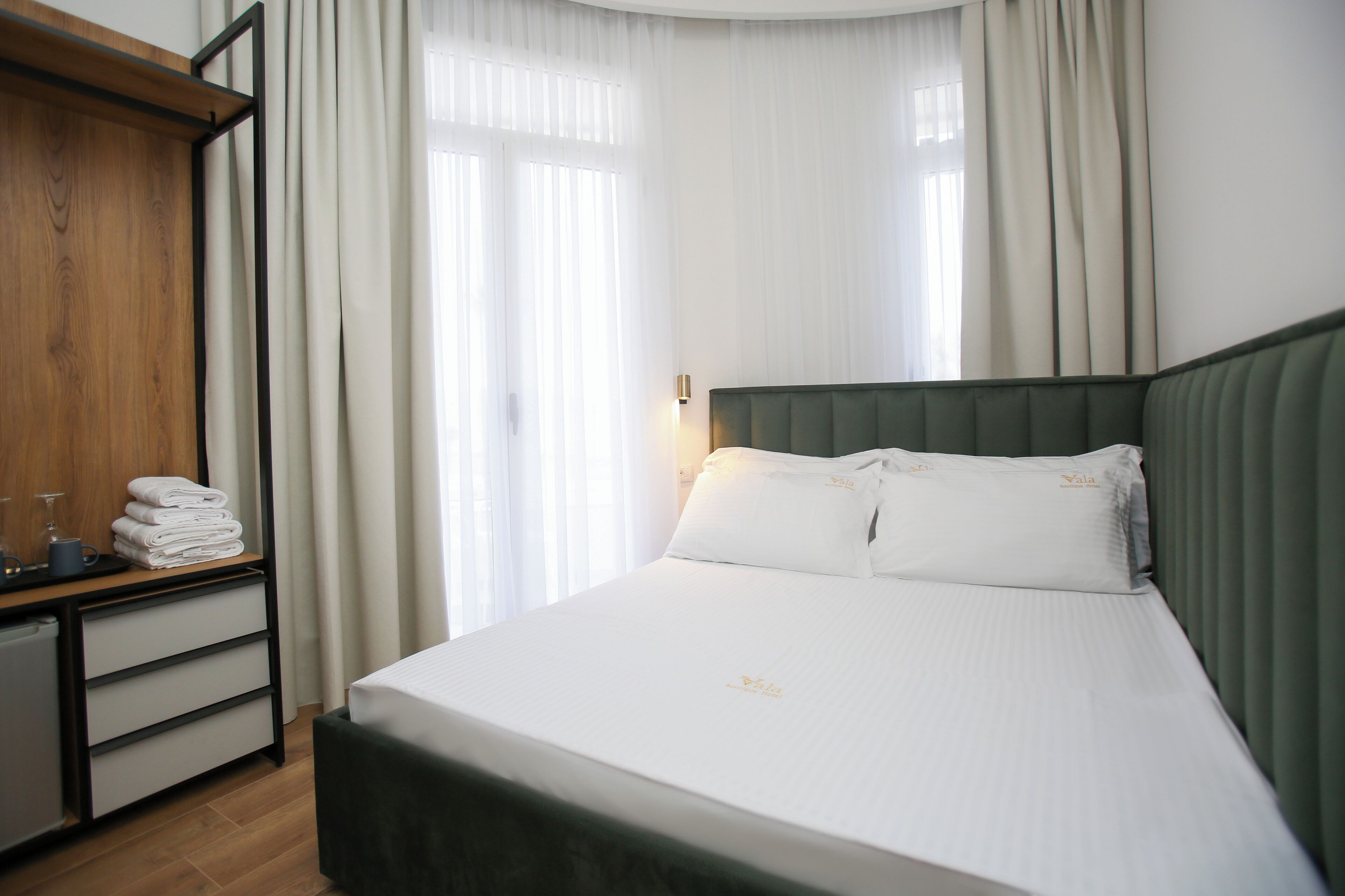 A neatly made bed with white linens, a wooden wardrobe, and a desk with a lamp.