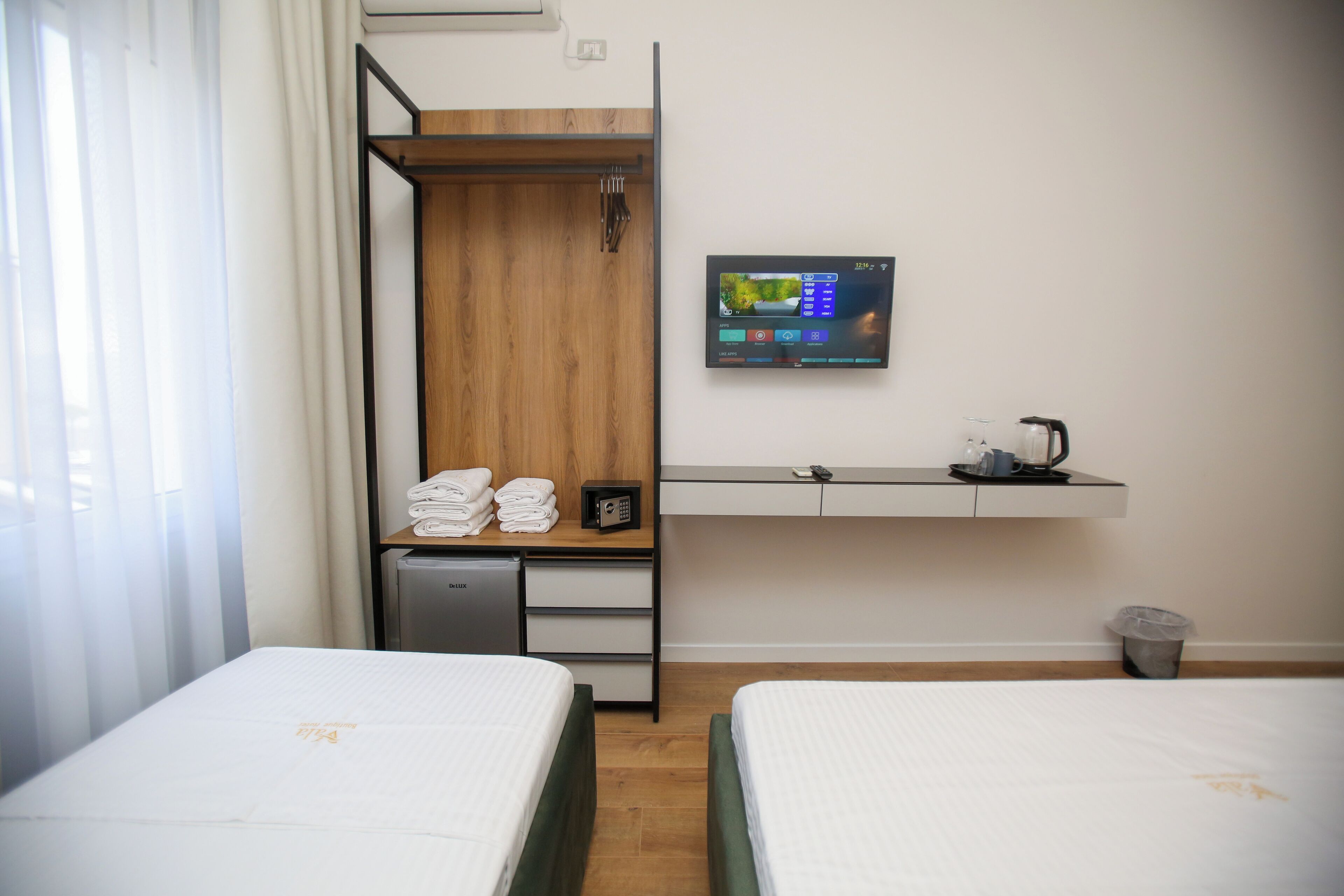 A hotel room with two beds, a small desk with a computer, a coffee maker, and a TV on the wall.