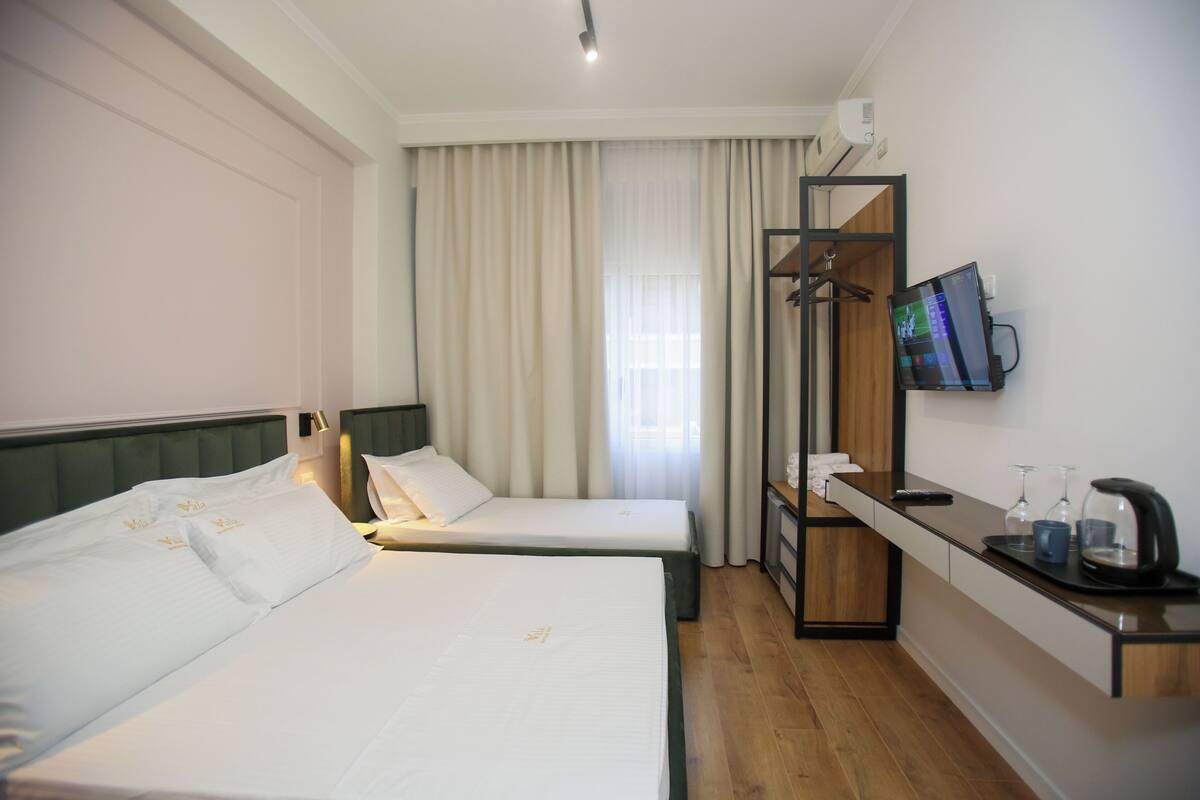 Habitación de hotel con dos camas, un escritorio con televisor y ventana con cortinas.