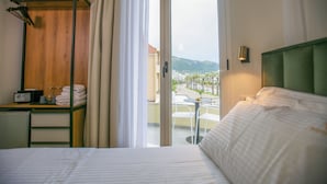 Habitación de hotel con cama, escritorio con teléfono y lentes, una silla y vistas al exterior.