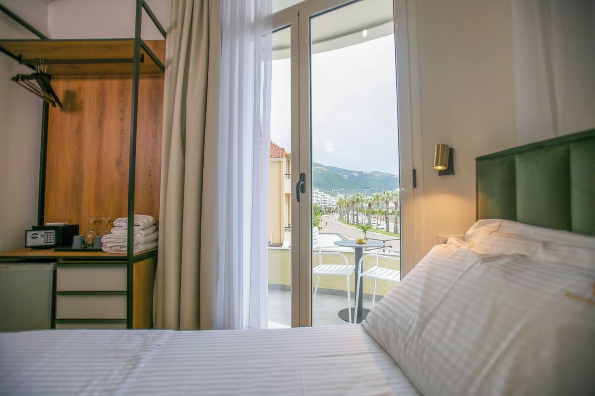 Habitación de hotel con cama, escritorio con teléfono y lentes, una silla y vistas al exterior.
