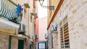 Una calle estrecha flanqueada por edificios, con balcones que muestran ropa tendida, unidades de aire acondicionado y un letrero de un negocio.
