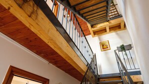Una escalera de madera con barandilla de metal, techo de madera y pared blanca con un cuadro enmarcado.