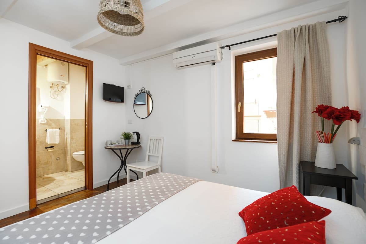 Habitación de hotel con cama, una mesita pequeña con una silla, televisor y ventana con cortinas.